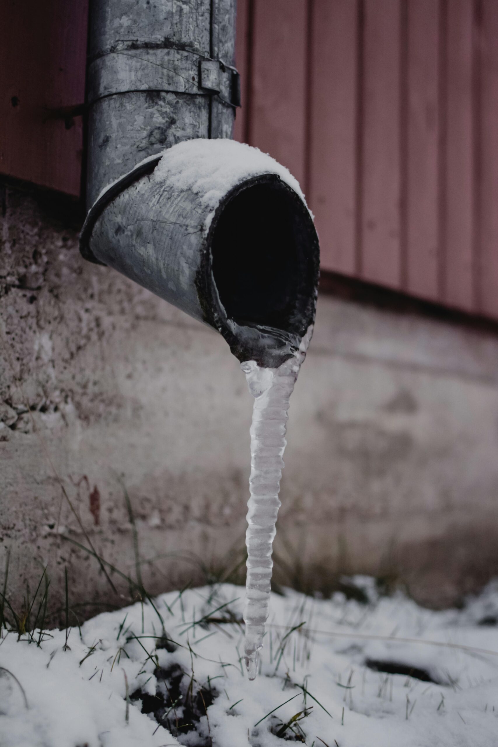Frozen drain spout with icicle against a snowy backdrop. Captured in Estonia.