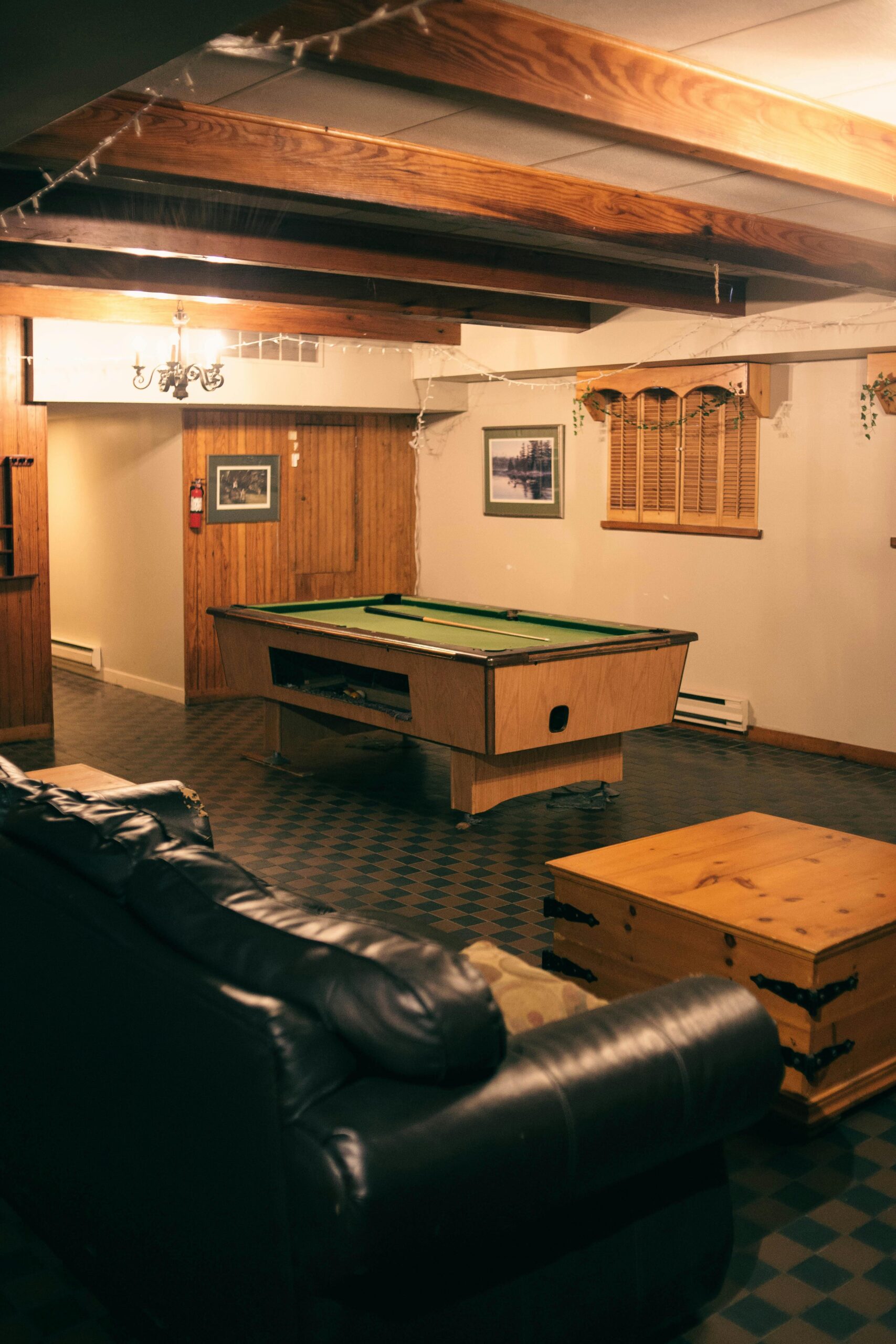 A warm and inviting basement game room featuring a pool table, couch, and wooden decor.