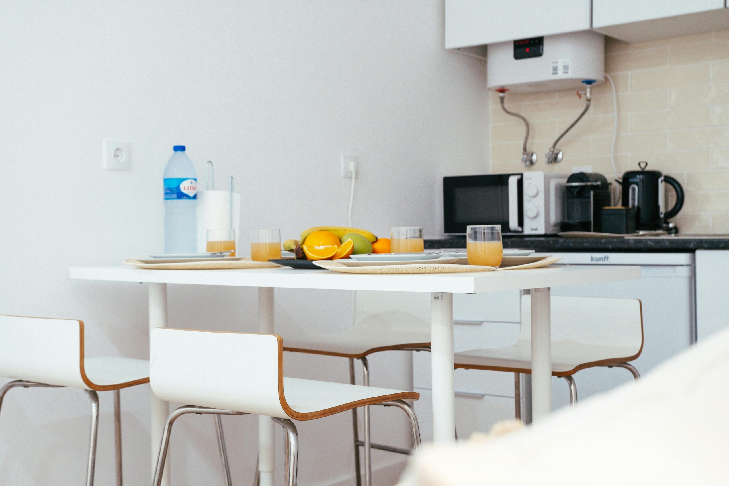 A modern kitchen with a neatly arranged table setting featuring fruit and juice, capturing a minimalist interior design.